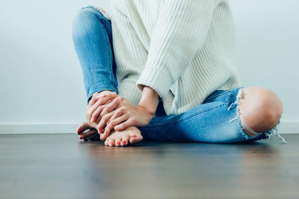 žena sjedi na podu i drži se grčevito za stopalo